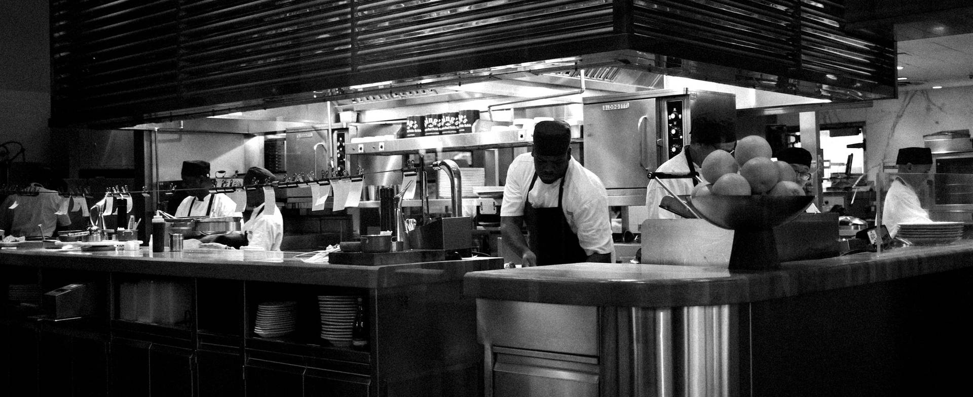 An open restaurant kitchen with the brigade at work, in black and white